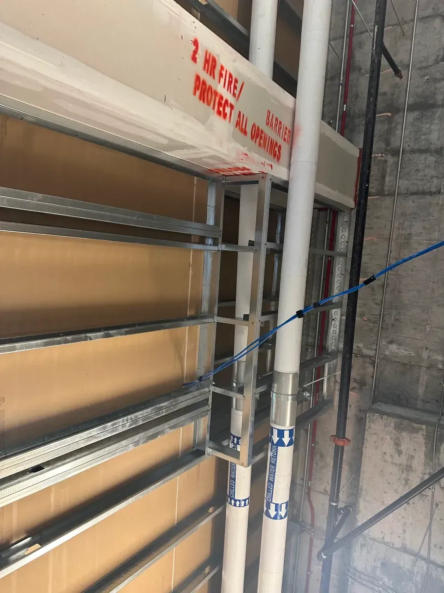 Pipes run along a metal grid with drywall above. Red text on drywall reads 