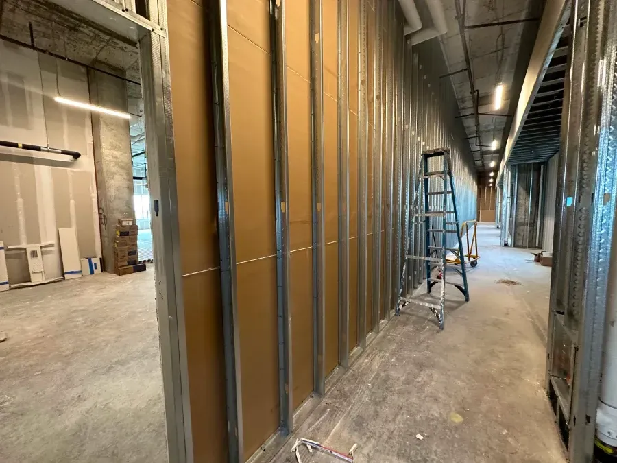 Interior construction: hallway with metal studs, brown insulation, and unfinished walls. A ladder leans against a wall.