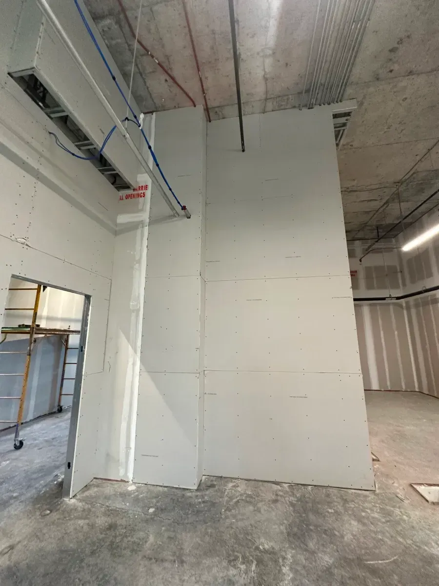 Interior construction scene. Drywall walls being built, exposed ceiling with wiring.