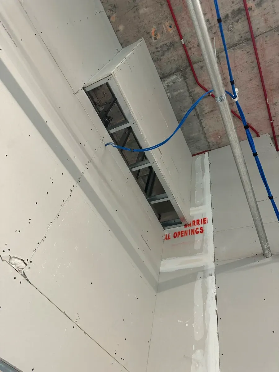 Ceiling with rectangular openings and exposed metal framing. Red and blue pipes present. 