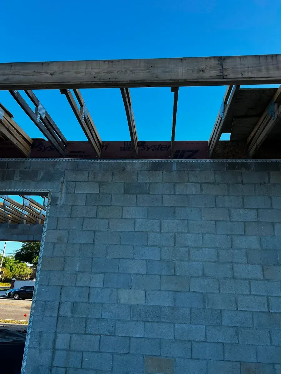 Partially built concrete block building with exposed wooden beams and a blue sky.