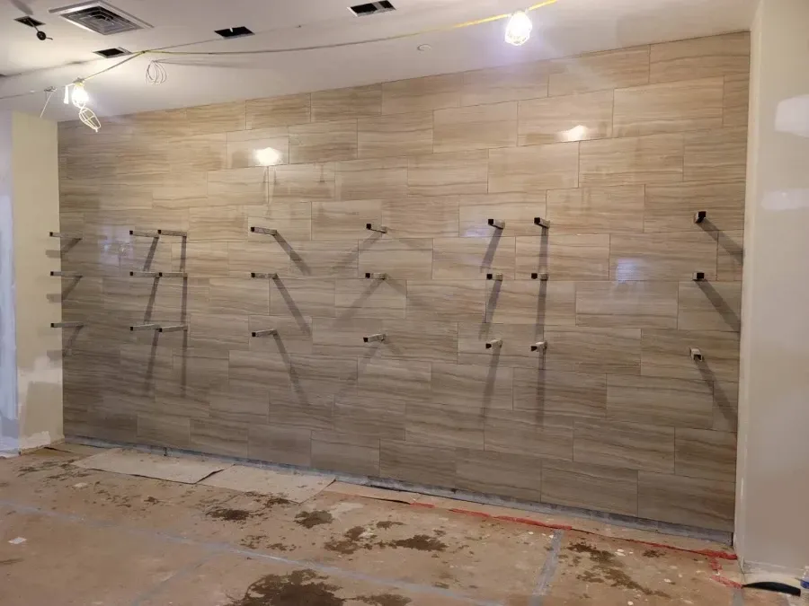 Wall tiled in light brown with metal support rods protruding, under construction.