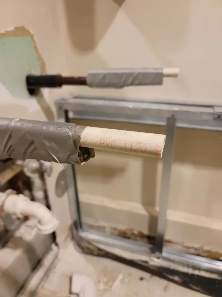 Two insulated pipes extend from a wall; a rectangular metal frame is in the background.