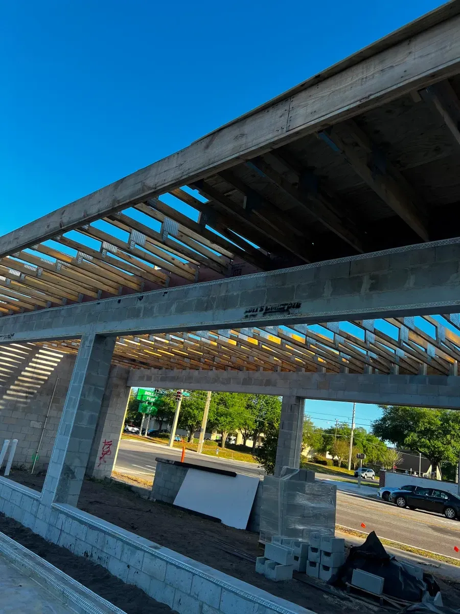 Construction of a concrete building with exposed wooden rafters. Bright sky.