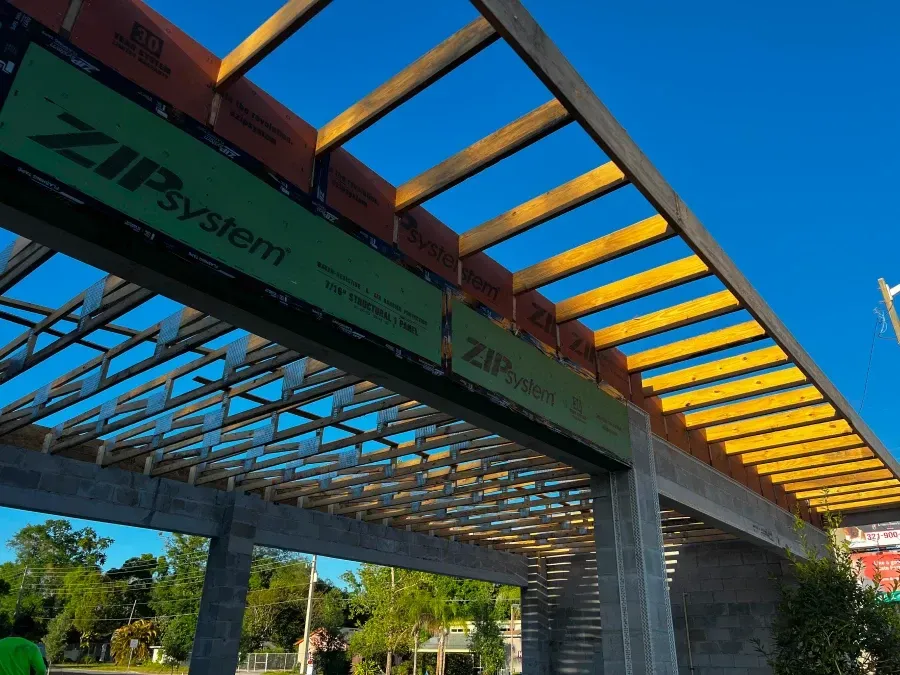 Wooden pergola under construction, with ZIP System boards, against a bright blue sky.