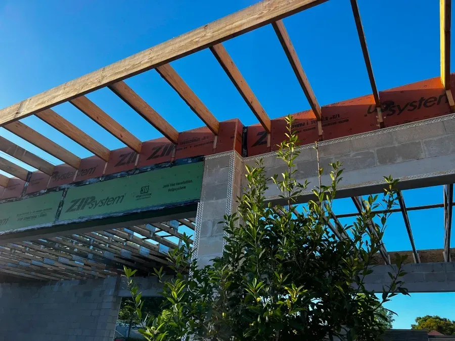 Construction site with wooden beams and green and orange sheathing against a blue sky.
