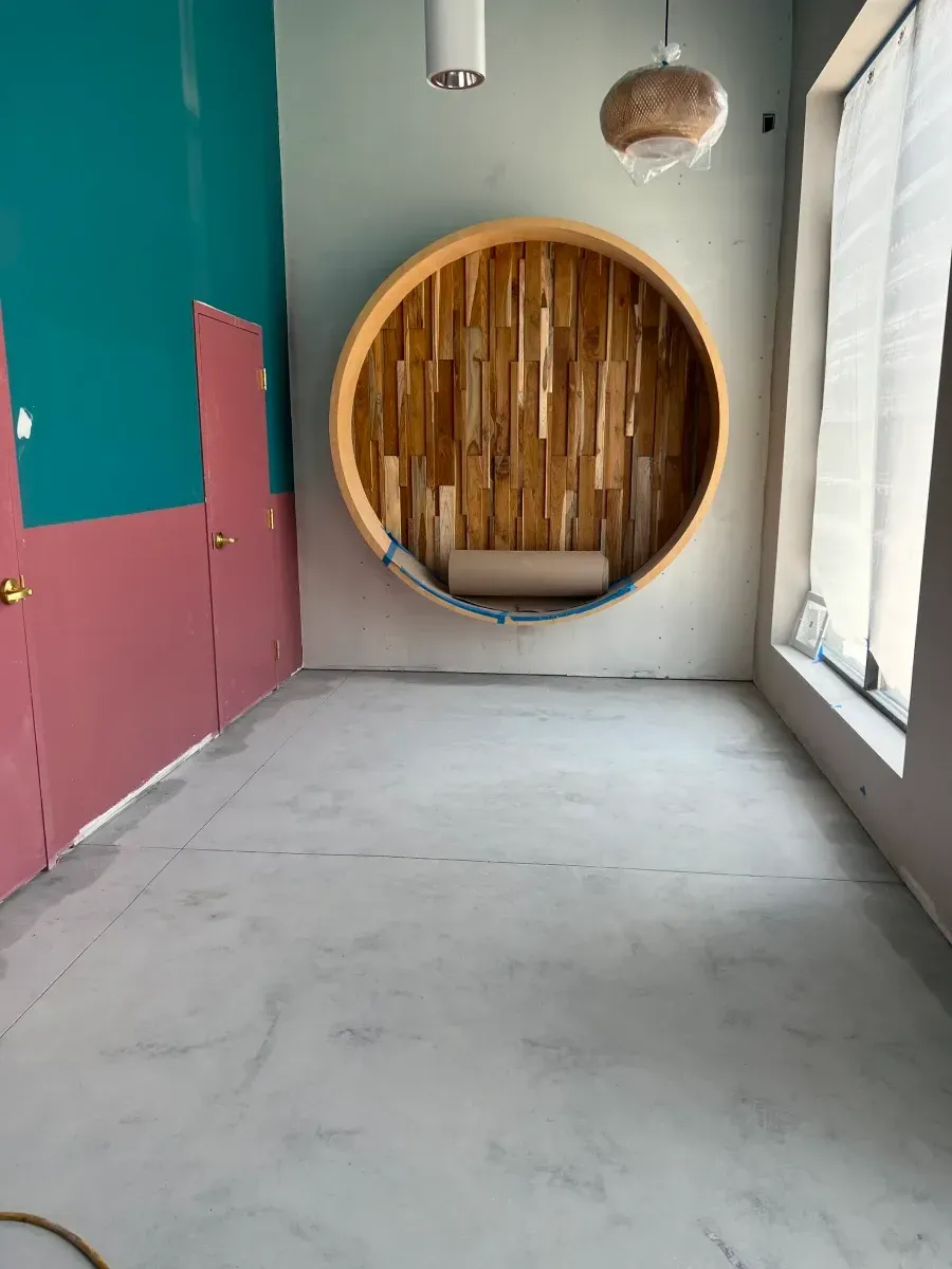 Empty room with teal and pink walls, wooden circular bench, and large window.