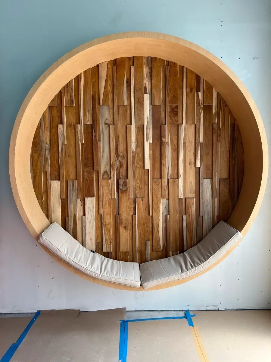 Circular wooden wall-mounted seating with wood plank back and gray cushions.