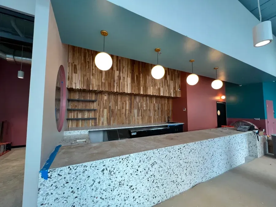 Interior of a new business with a speckled countertop, wooden wall, shelves, and pendant lights.