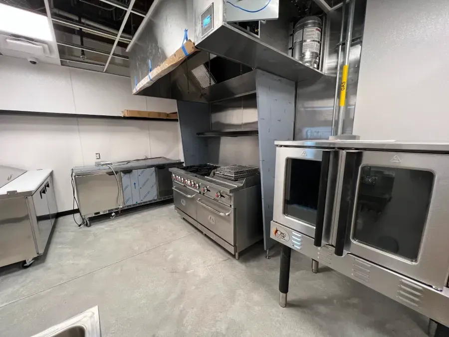 Commercial kitchen with stainless steel appliances: oven, stove, vent hood, and counters.