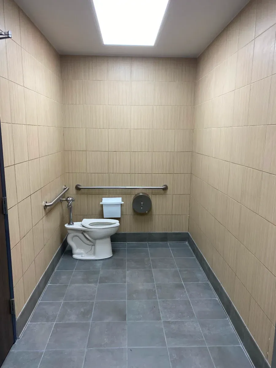 Accessible restroom with toilet, grab bars, and neutral-colored tile walls and floor.