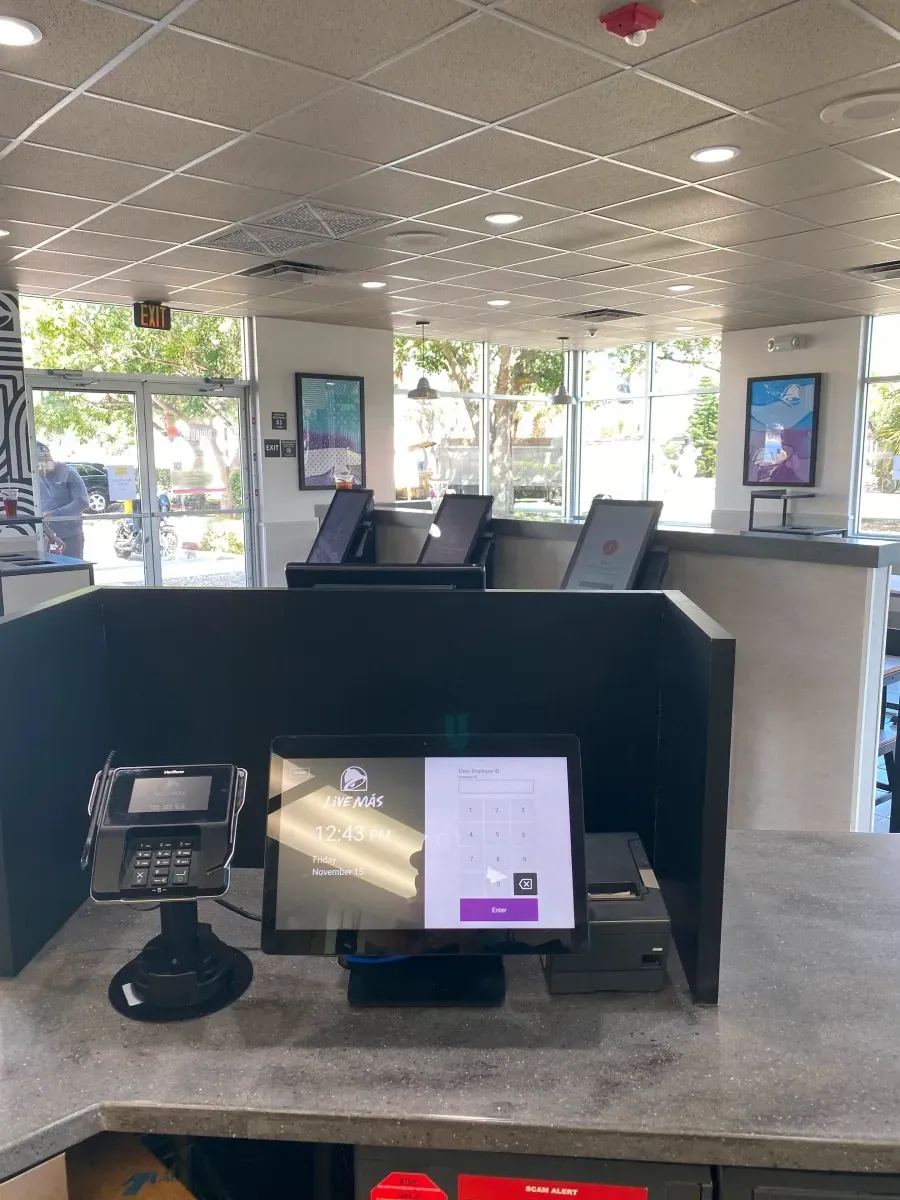 Taco Bell counter with digital kiosks and payment terminal.