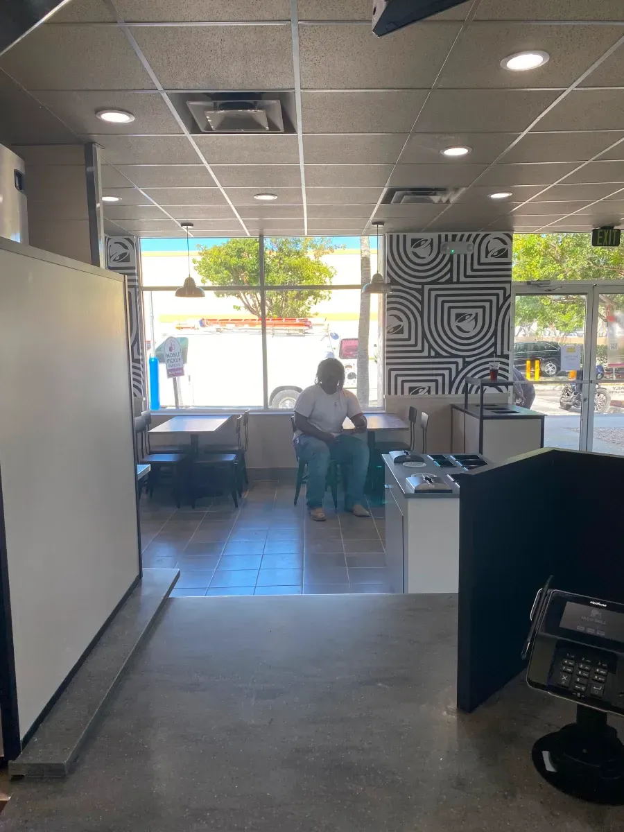 Restaurant interior with person seated at a table near a window; black and white patterned wall art visible.