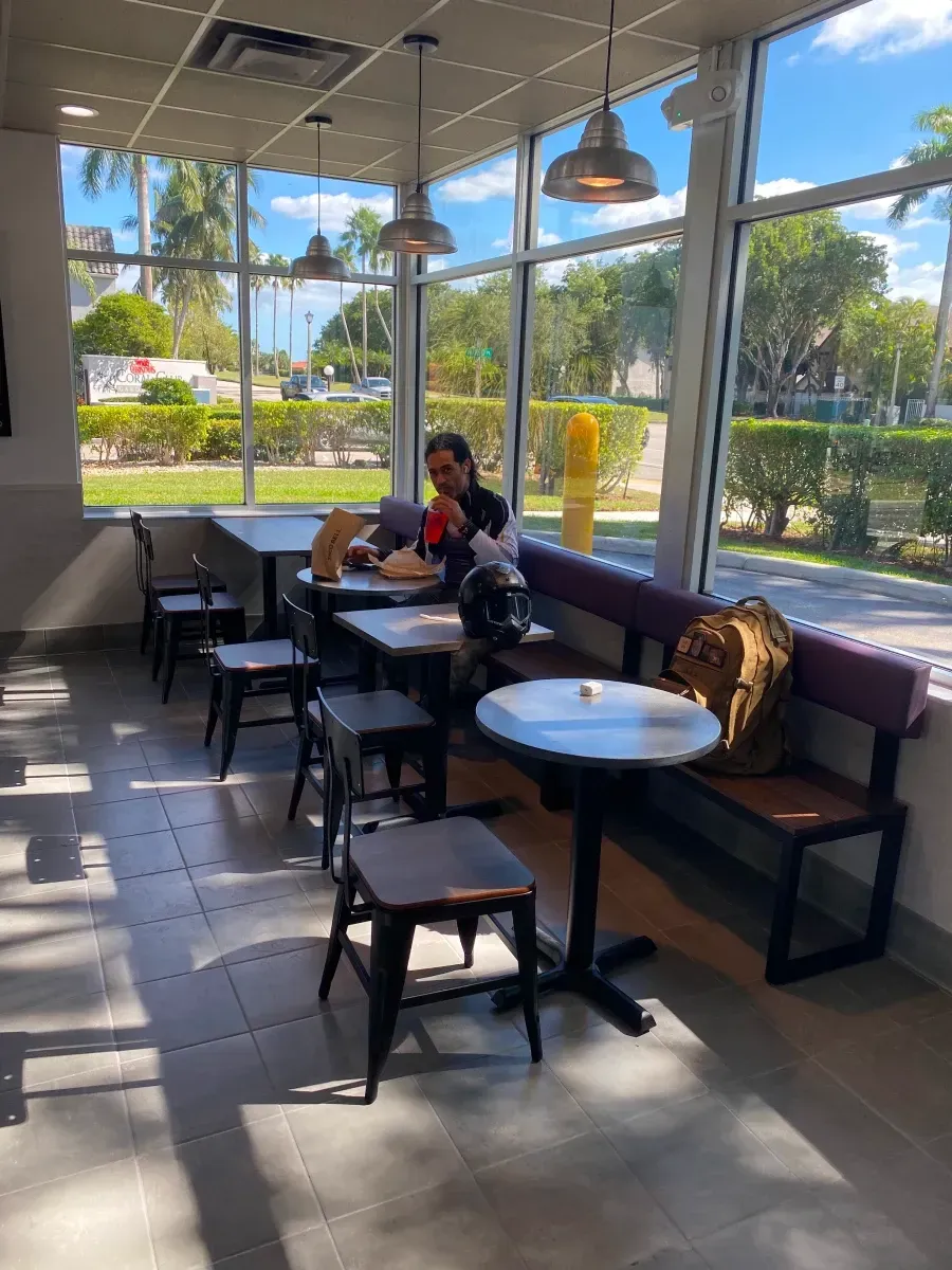 Restaurant interior with person at table, purple bench, windows, natural light.