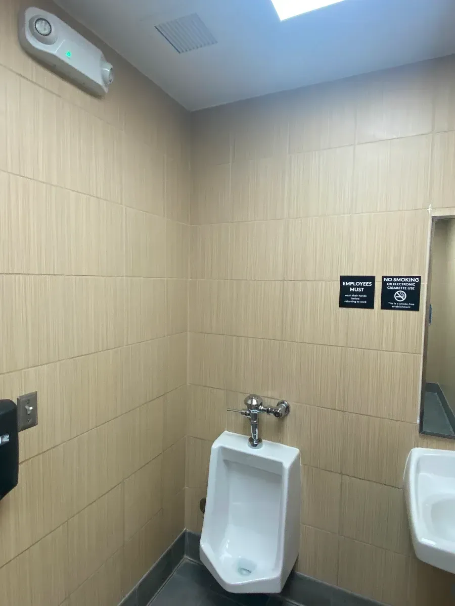 Public restroom with urinal, sink, and beige tiled walls.