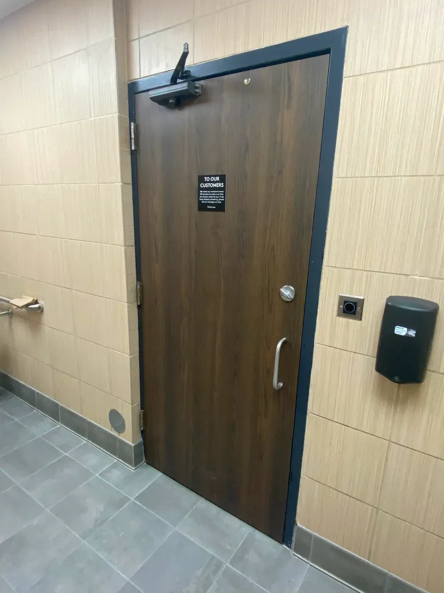 Brown door with black trim, accessible restroom, automatic door opener.