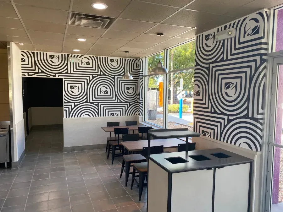 Interior of a Taco Bell with black and white patterned walls, tables, chairs, and large windows.