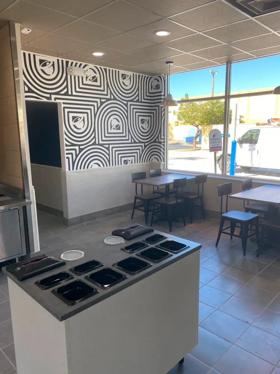 Interior of a modern restaurant, featuring a food prep counter, tables, chairs, and patterned wall decor.
