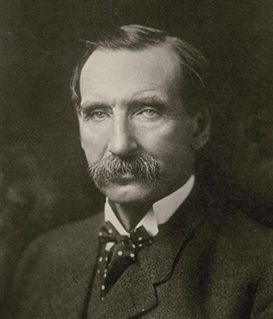 Portrait of a man with a mustache, wearing a suit and a polka-dot bowtie against a dark background.