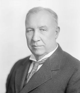 A studio portrait of a man in a dark suit, light shirt, and patterned tie against a plain white background.