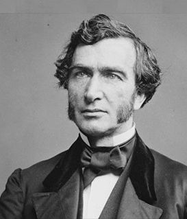 A studio portrait of Justus von Liebig, shown from the chest up, wearing a dark coat and bow tie against a gray background.