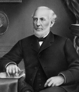 Black and white portrait of a formal gentleman in a suit and waistcoat, seated at a desk with his hand resting on a book.