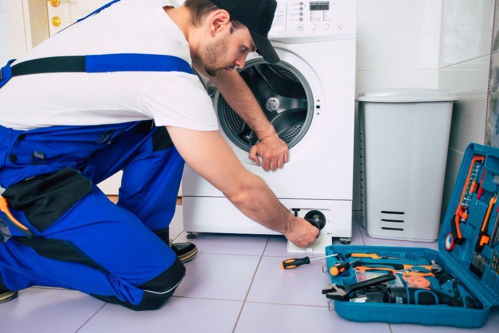 A Man Is Fixing A Washing Machine In A Laundry Room