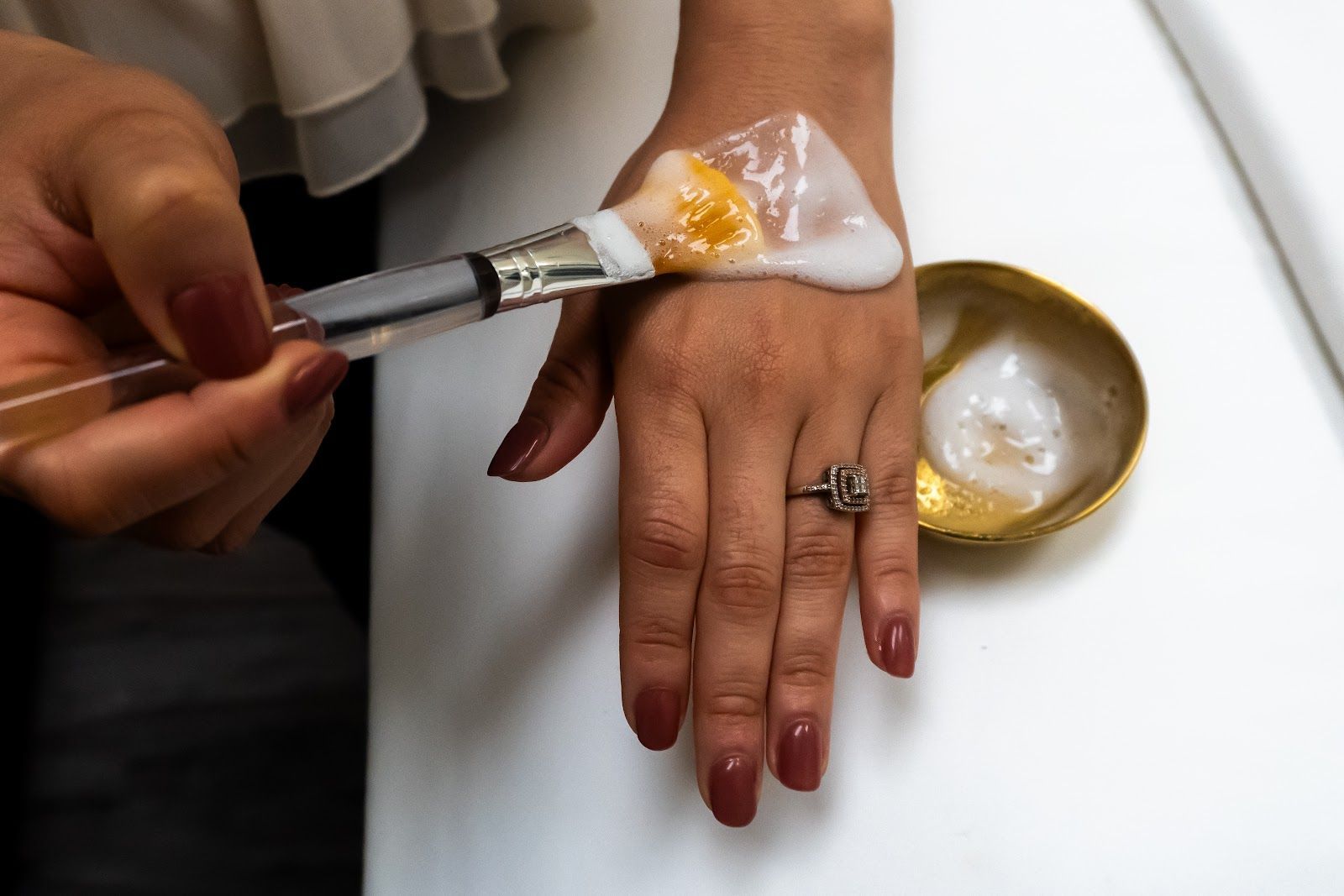 A woman is applying a cream to her hand with a brush.