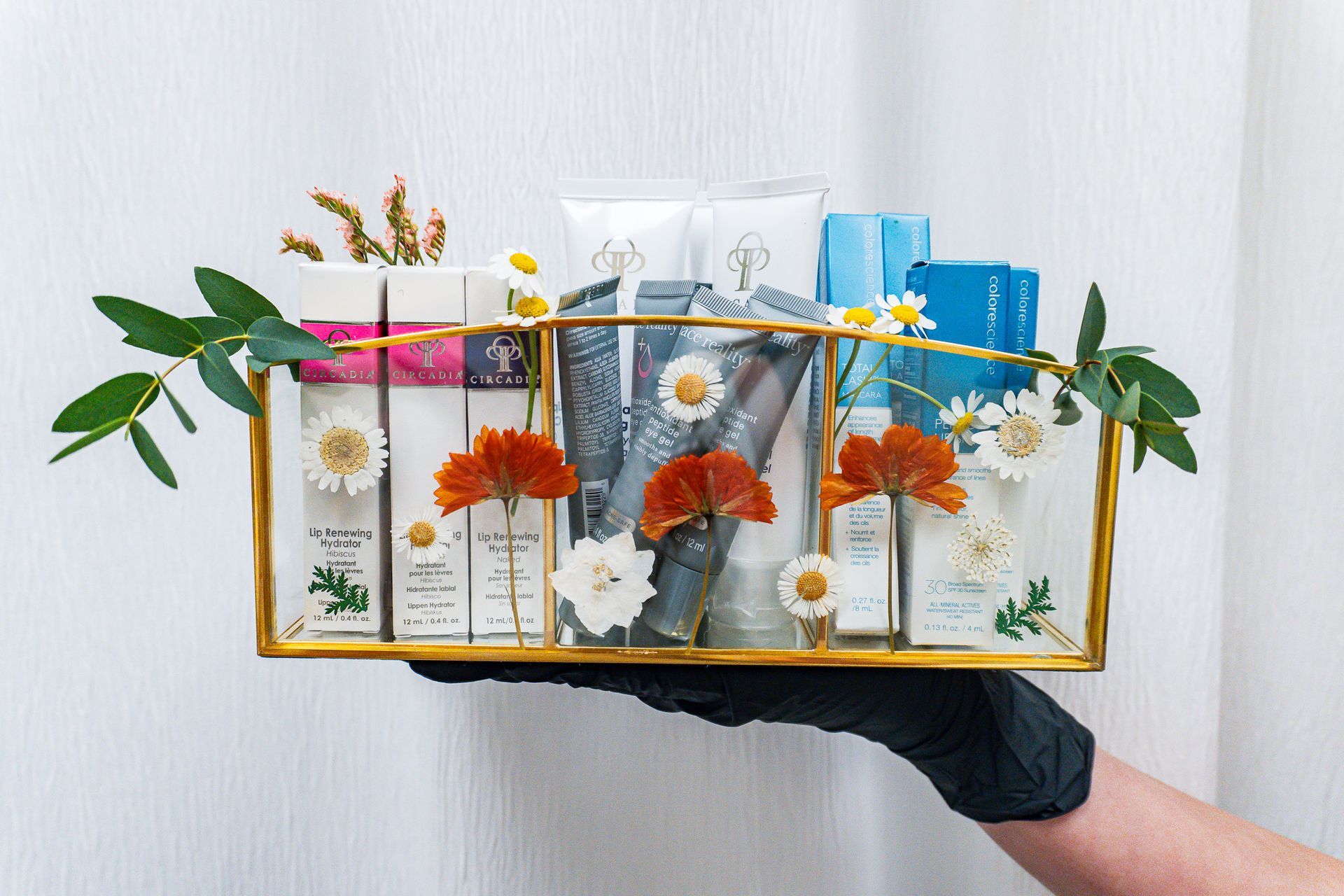 A person is holding a glass tray filled with cosmetics and flowers.