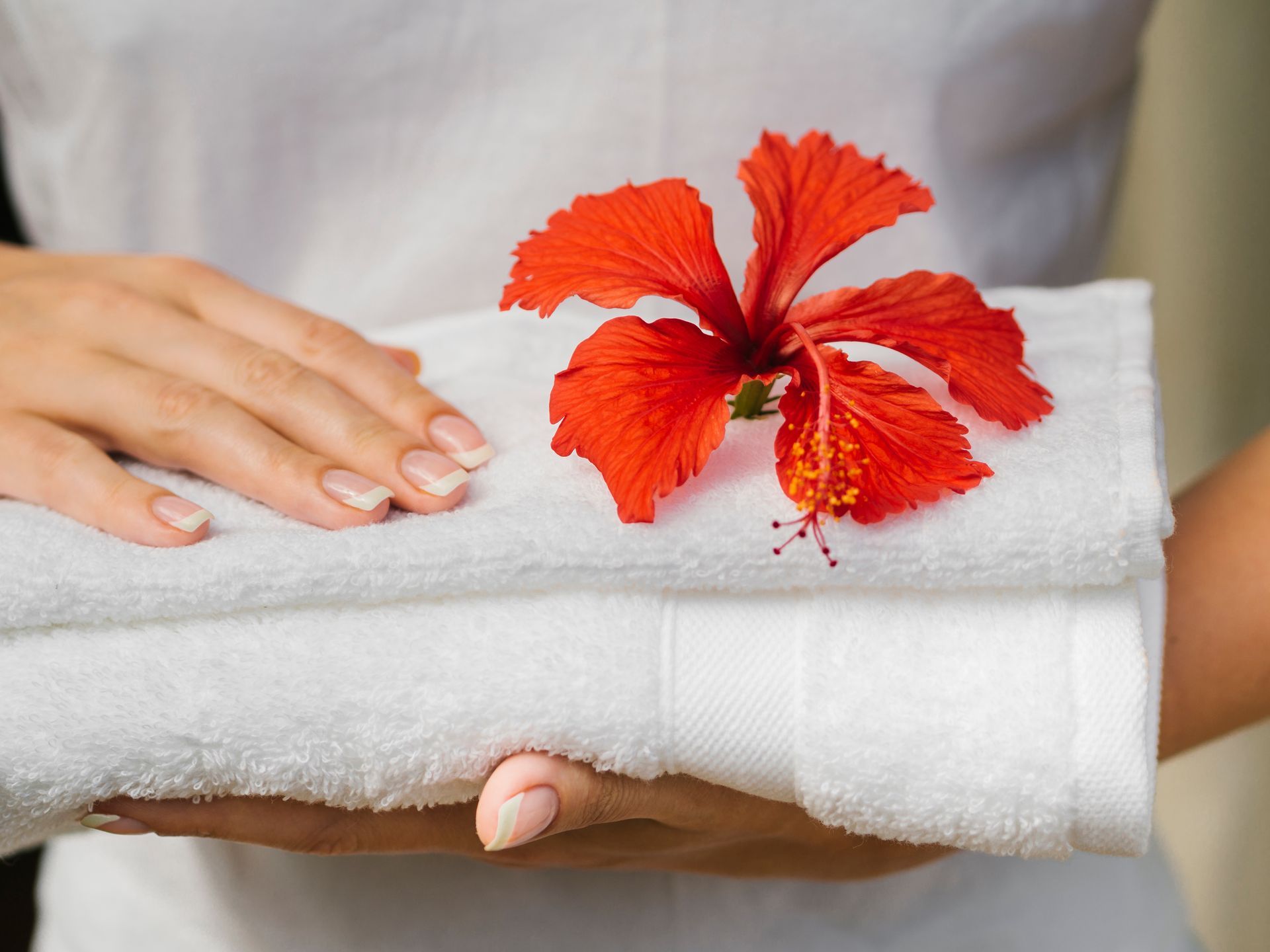 A woman is holding a stack of towels with a red flower on top.