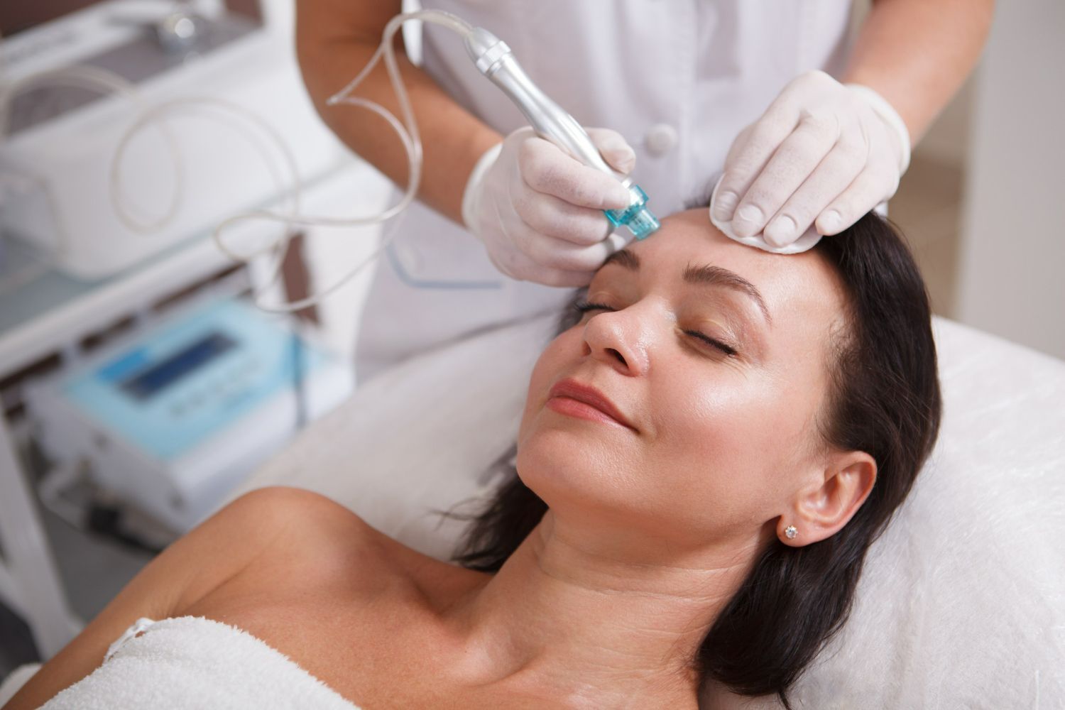 Woman receiving facial treatment in a clinic; a medical professional holds a device on her forehead.