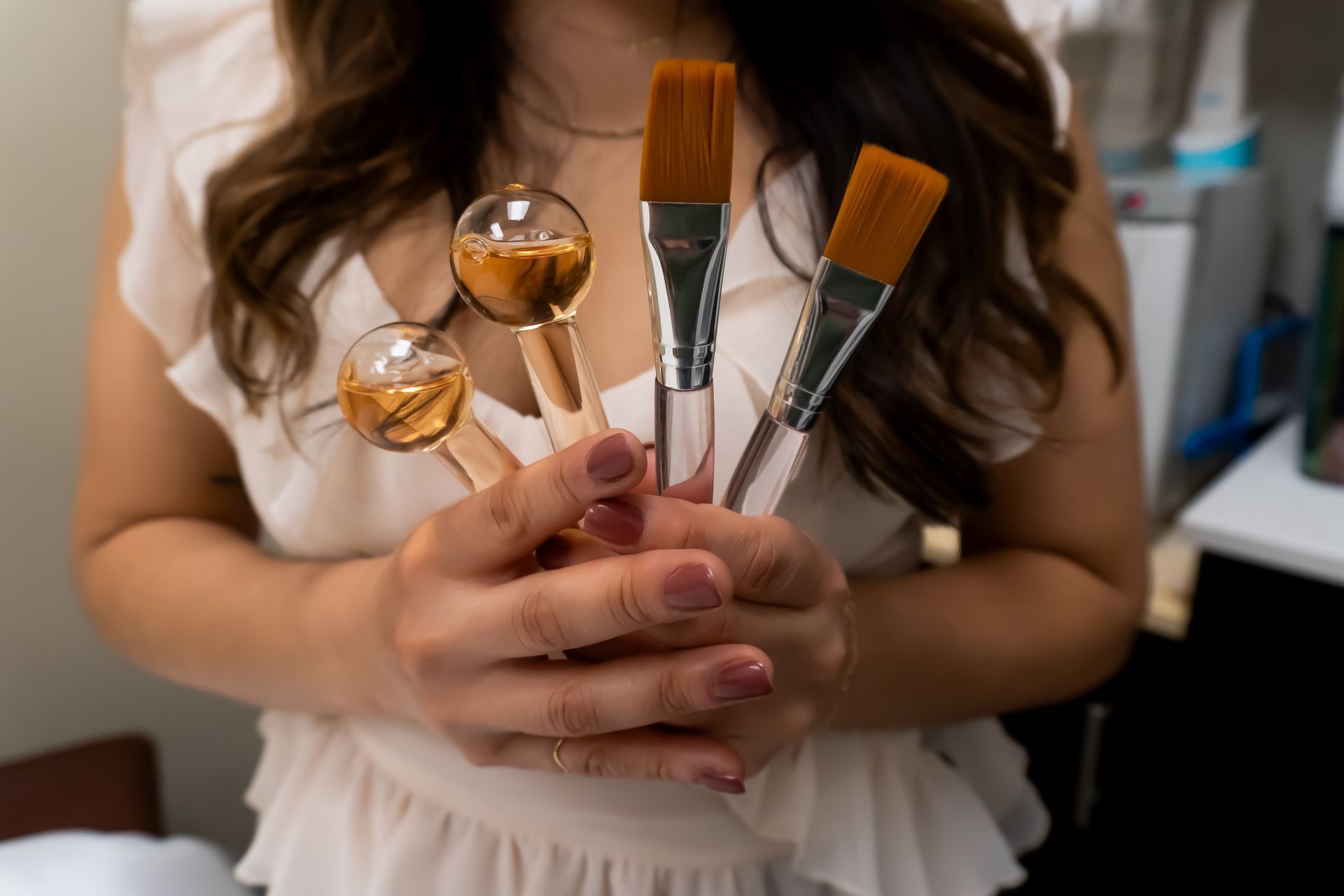 A woman is holding three makeup brushes in her hands.