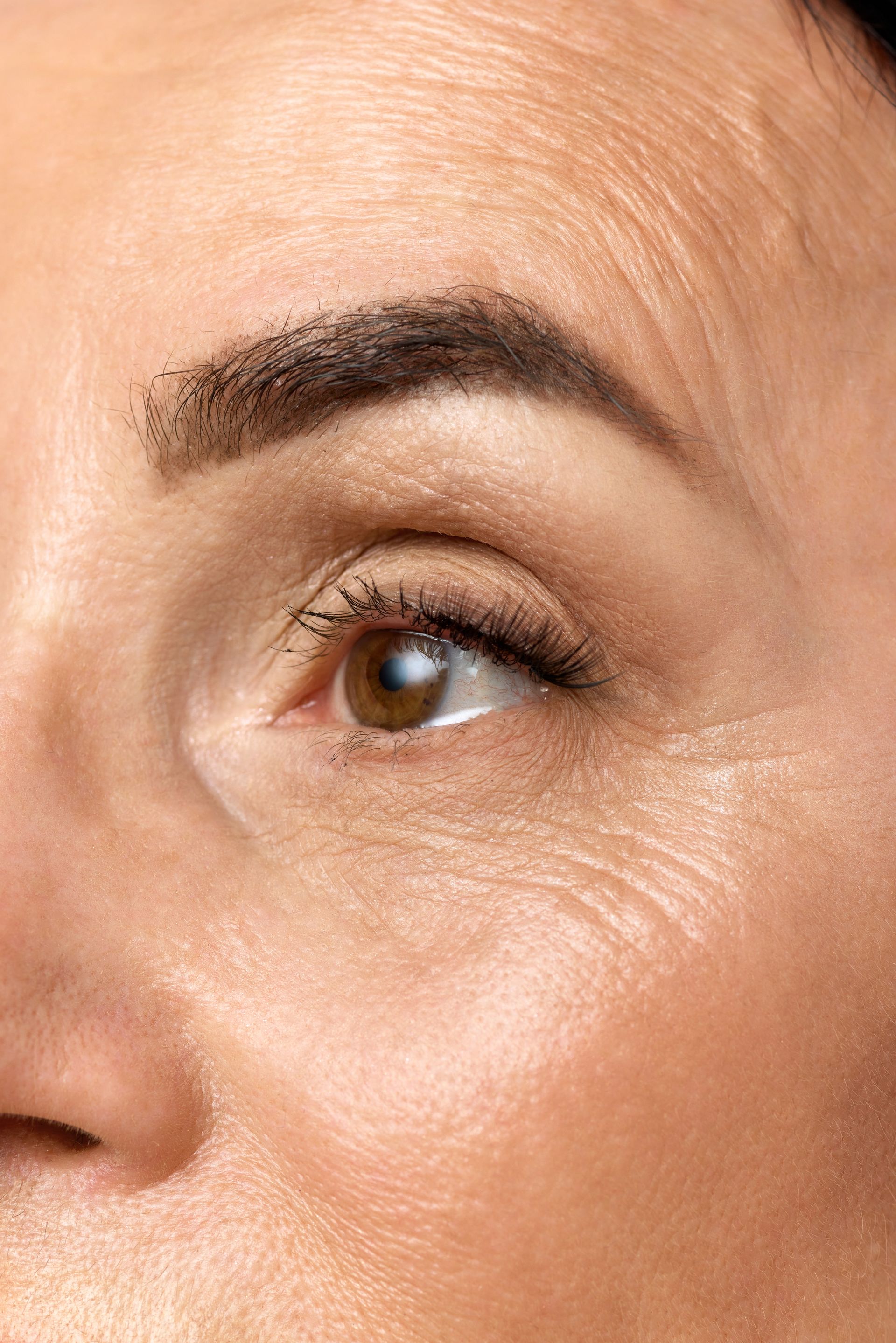 Close-up of a person's eye with wrinkles, showing the eyebrow, eyelid, and crow's feet.