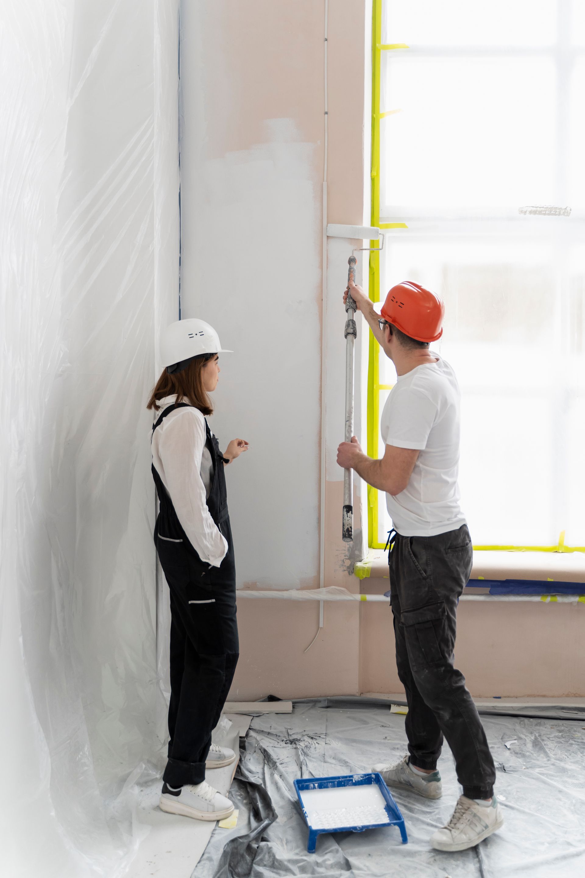 A man and a woman are painting a wall in a room.
