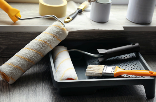 A tray of paint rollers and brushes on a wooden table.