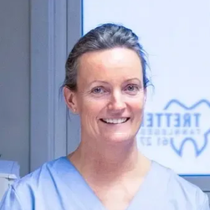 Kvinne i blå skrubber smiler, på et tannlegekontor.