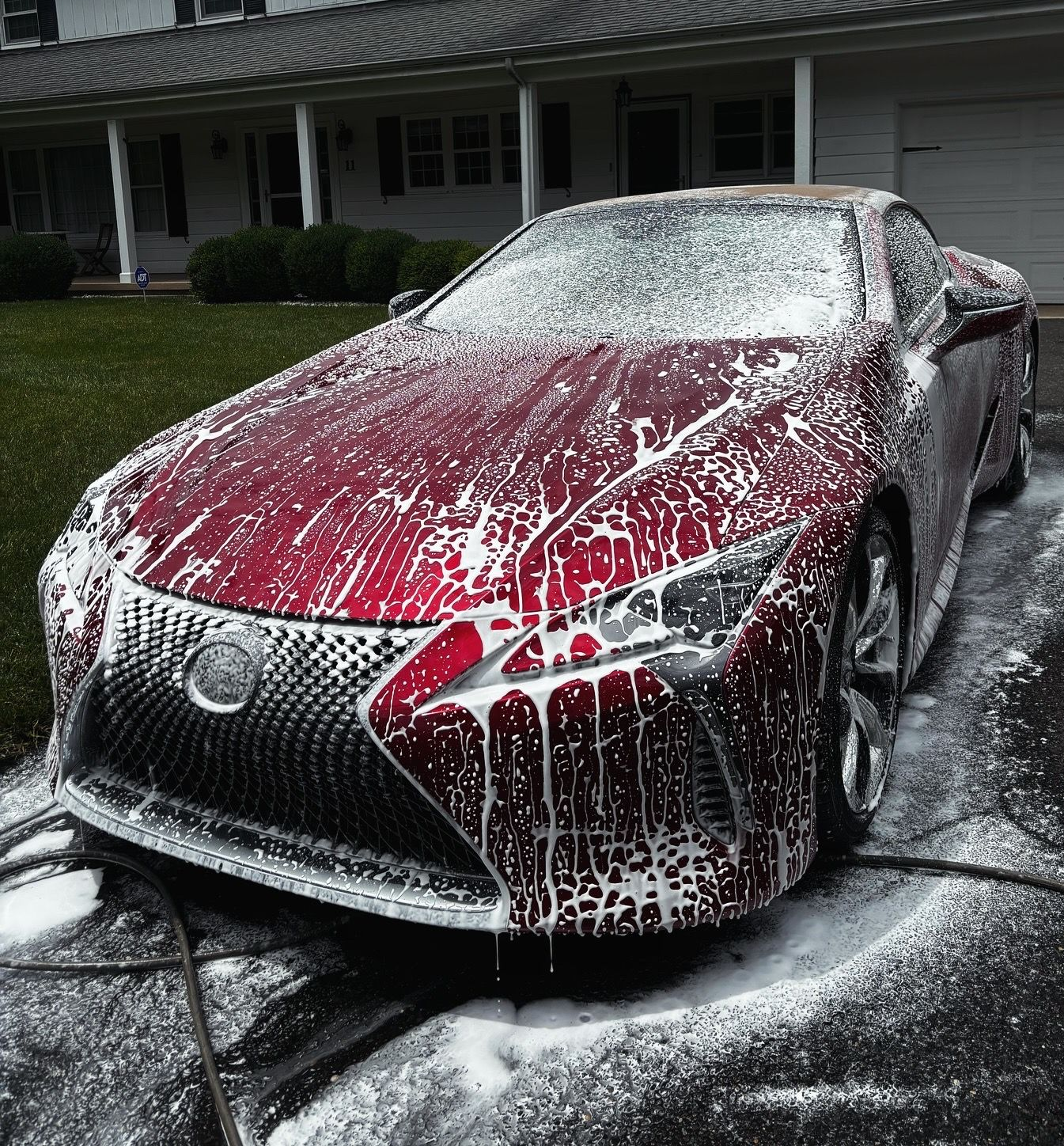 Red sports car covered in foam during hand wash detailing at client’s home.