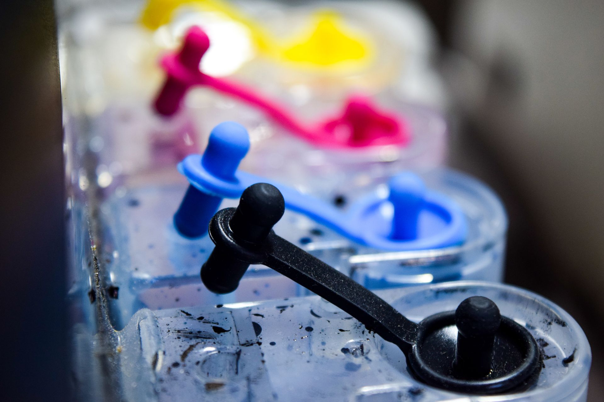 Close-up of printer ink tank caps in cyan magenta yellow and black colors on refill use