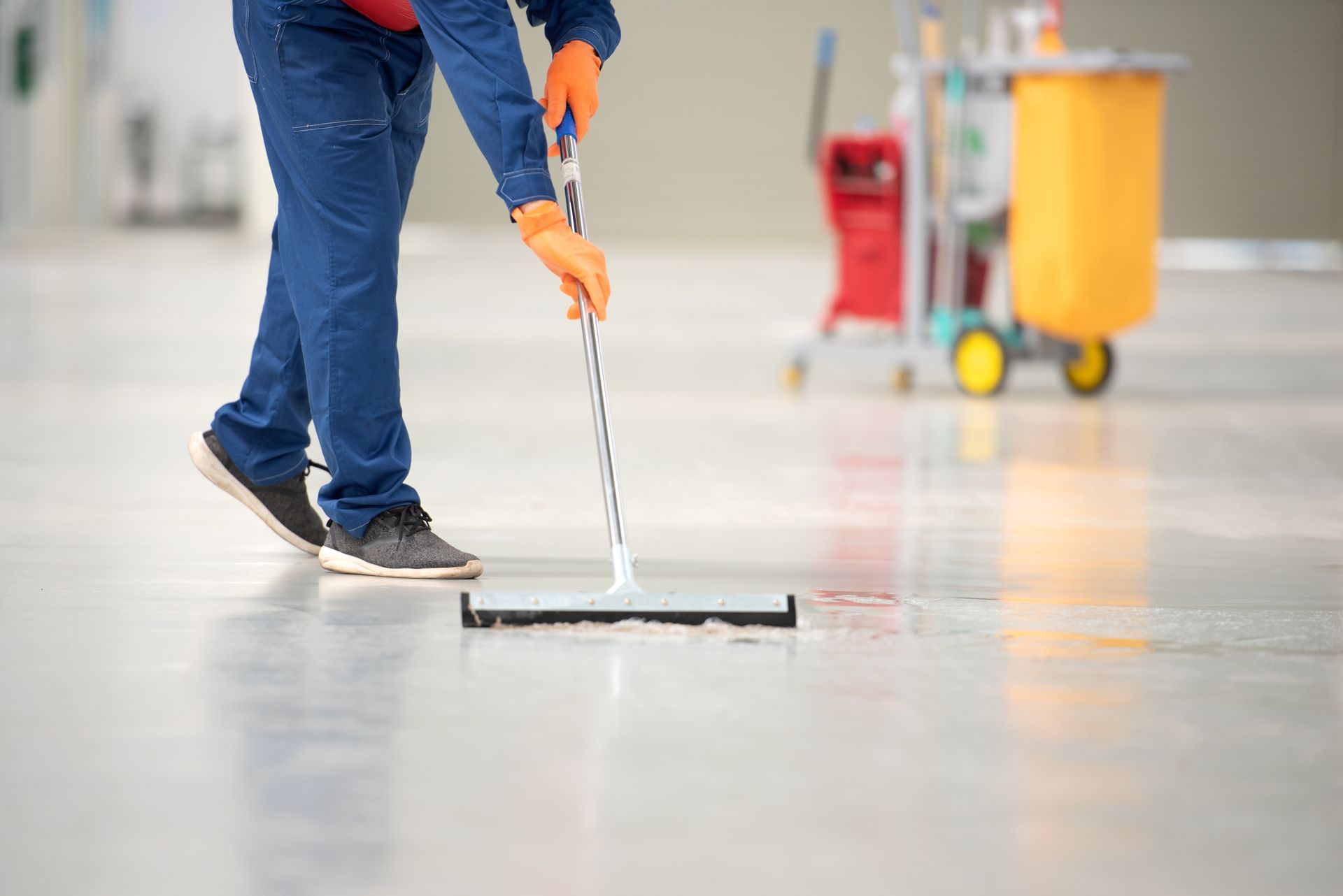 Worker using a floor squeegee to clean a large wet surface indoors. Worker using a floor squeegee to clean a large wet surface indoors.