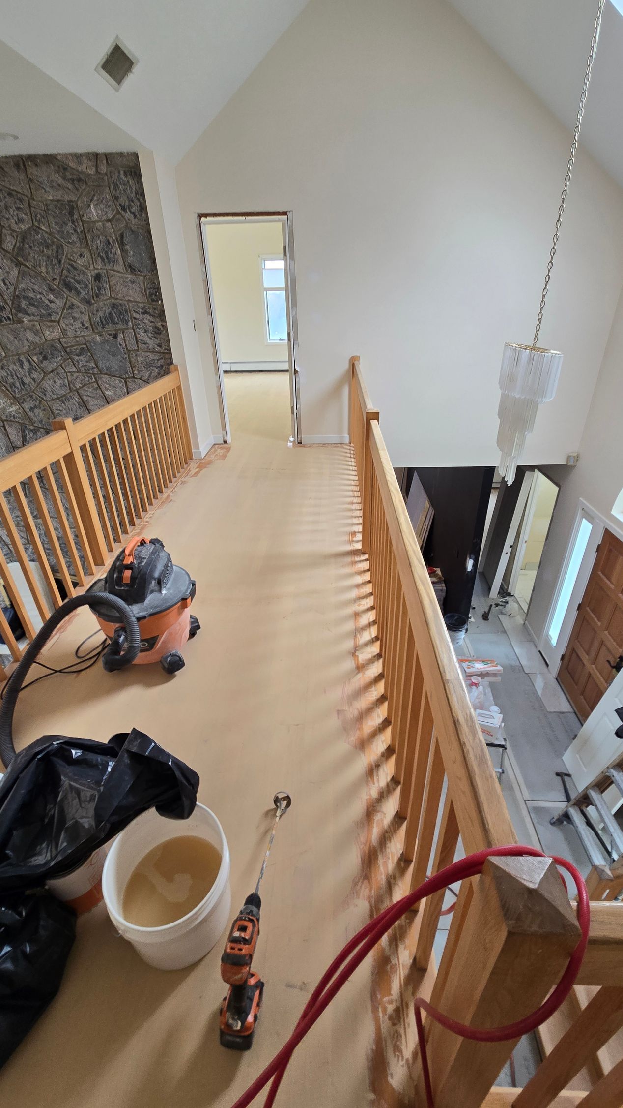 Interior shot of a hallway balcony with a wood railing, leading to a doorway, overlooking a lower floor.