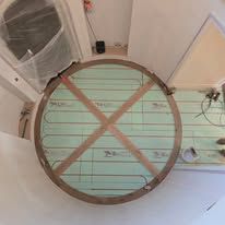 Circular floor with green insulation, heating coils, and wooden cross braces in a room.