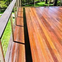 Wooden deck with a dark stripe, metal railings, and a green backdrop.