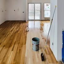 Newly stained wooden floor with bucket, roller, and brush in a room.