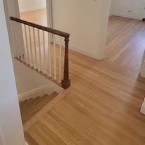Wooden staircase and flooring in a house, with white railing and natural wood tones.