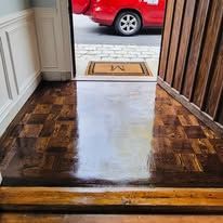 View from doorway onto glossy parquet floor, red car visible outside.