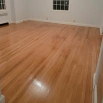 Hardwood floor in an empty room, light wood, natural lighting, and a white border around the room.