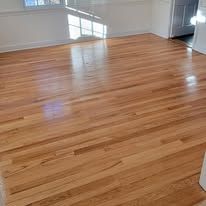 Shiny, light-brown hardwood flooring in a room with a window and white walls.