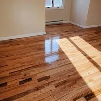 Shiny hardwood floor with sunlight reflecting, near a window and white wall.