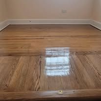 Close-up of a hardwood floor with a glossy finish. Light brown wood grain reflects light.
