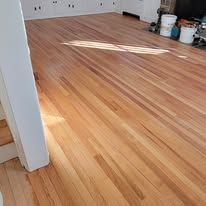 Hardwood floor, light brown with subtle grain, in a room with a white column and light streaming across it.